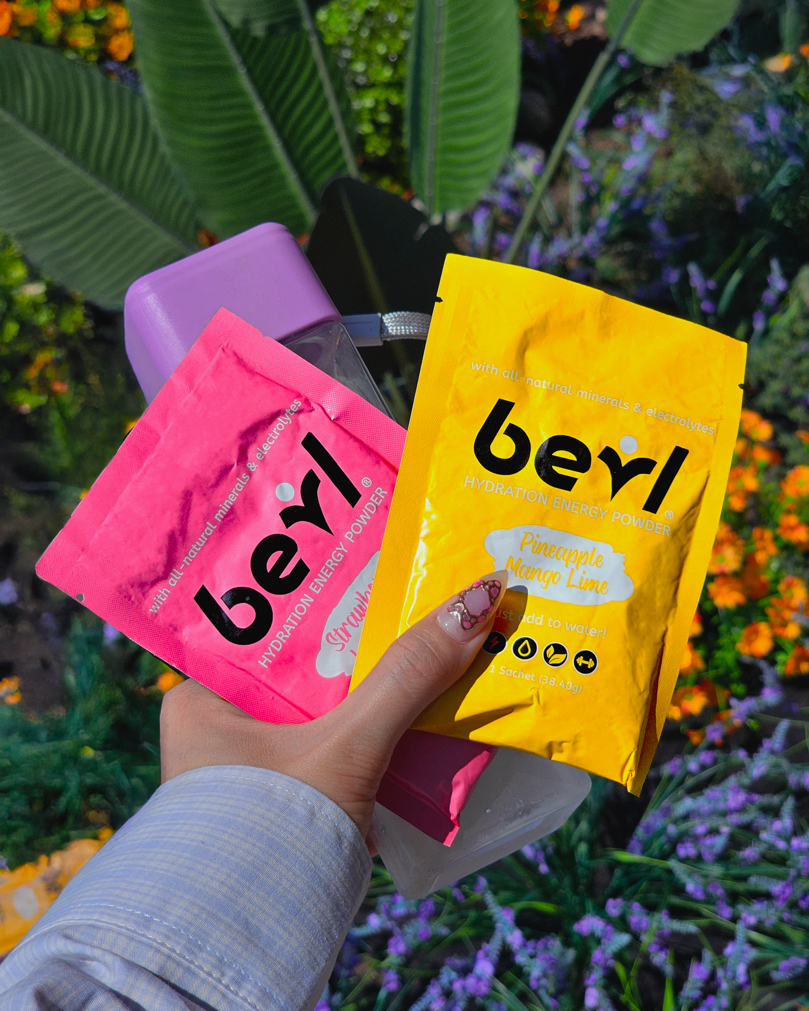 Hand holding pink and yellow 'beyl' packets against a natural background with plants and flowers.
